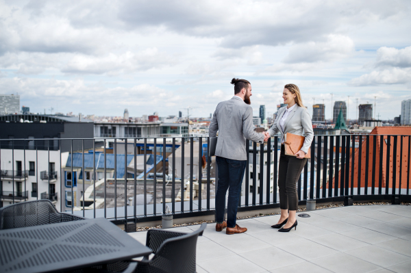 Two young businesspeople standing on a terrace outside office, shaking hands.