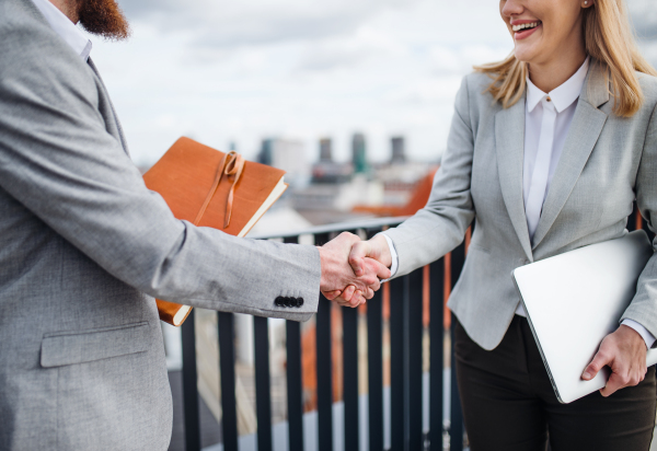 Midsection of two young businesspeople standing on a terrace outside office, shaking hands.