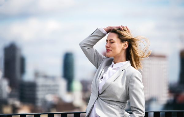 A portrait of young blond businesswoman standing outdoors on terrace outside office. Copy space.