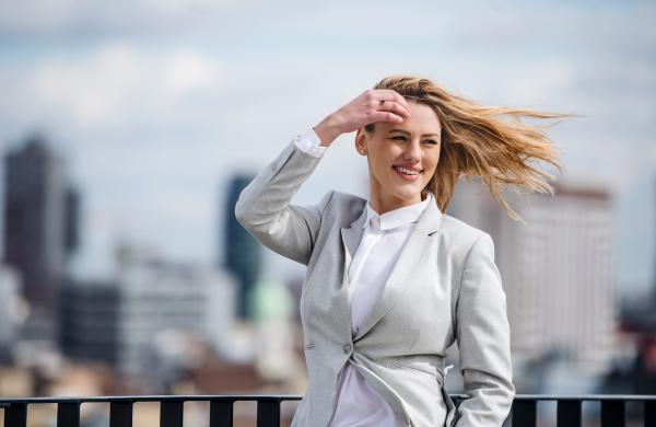 A portrait of young blond businesswoman standing outdoors on terrace outside office. Copy space.