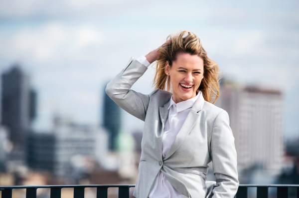 A portrait of young blond businesswoman standing outdoors on terrace outside office. Copy space.