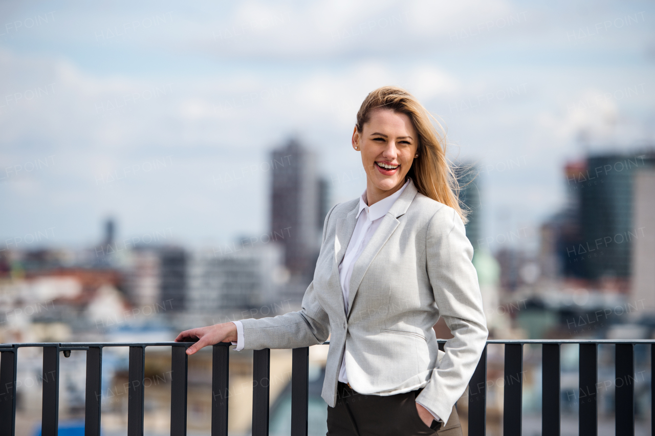 A portrait of young blond businesswoman standing outdoors on terrace outside office. Copy space.