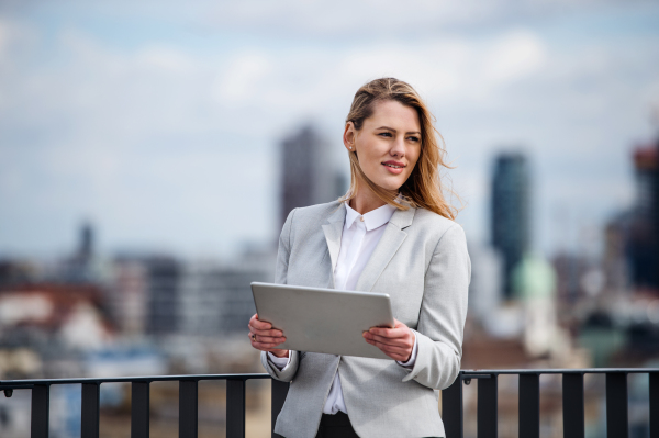 A young happy businesswoman with tablet standing on a terrace, working.