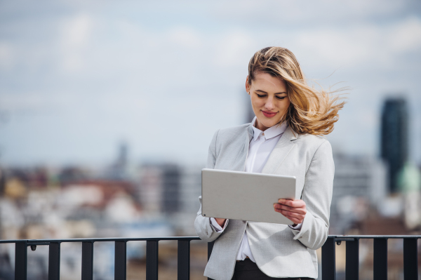 A young happy businesswoman with tablet standing on a terrace, working.