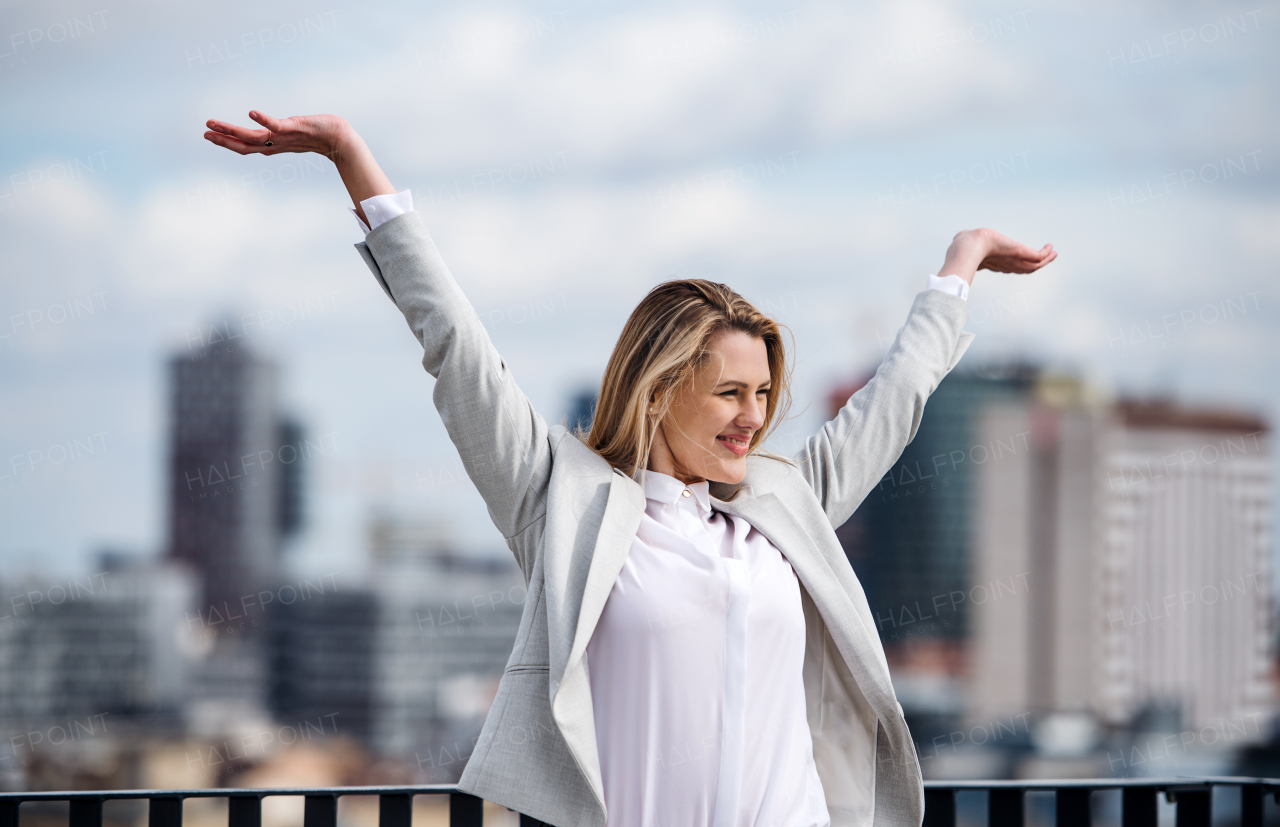 A young businesswoman standing on a terrace outside office, expressing excitement.