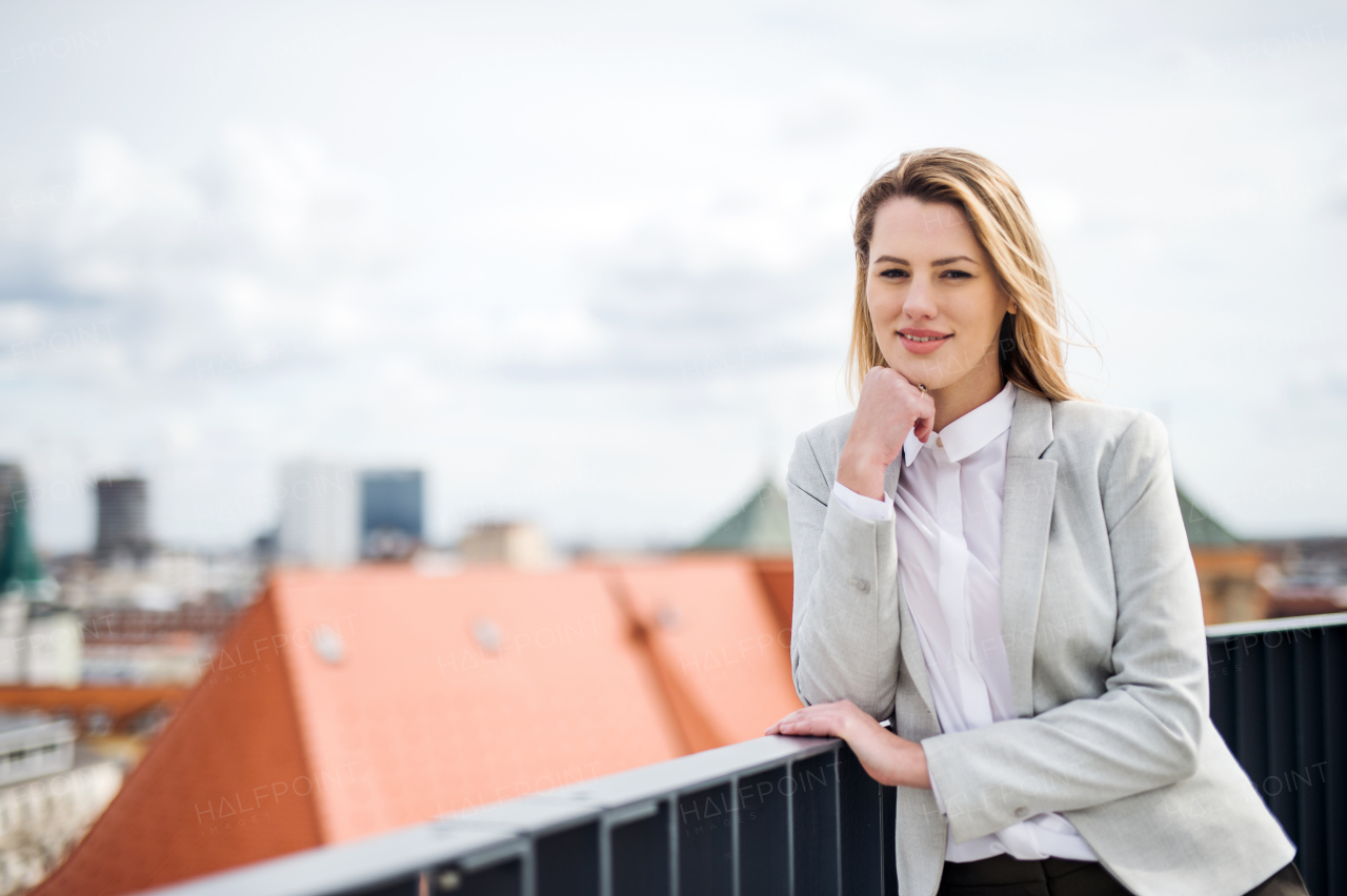 A portrait of young blond businesswoman standing outdoors on terrace outside office. Copy space.