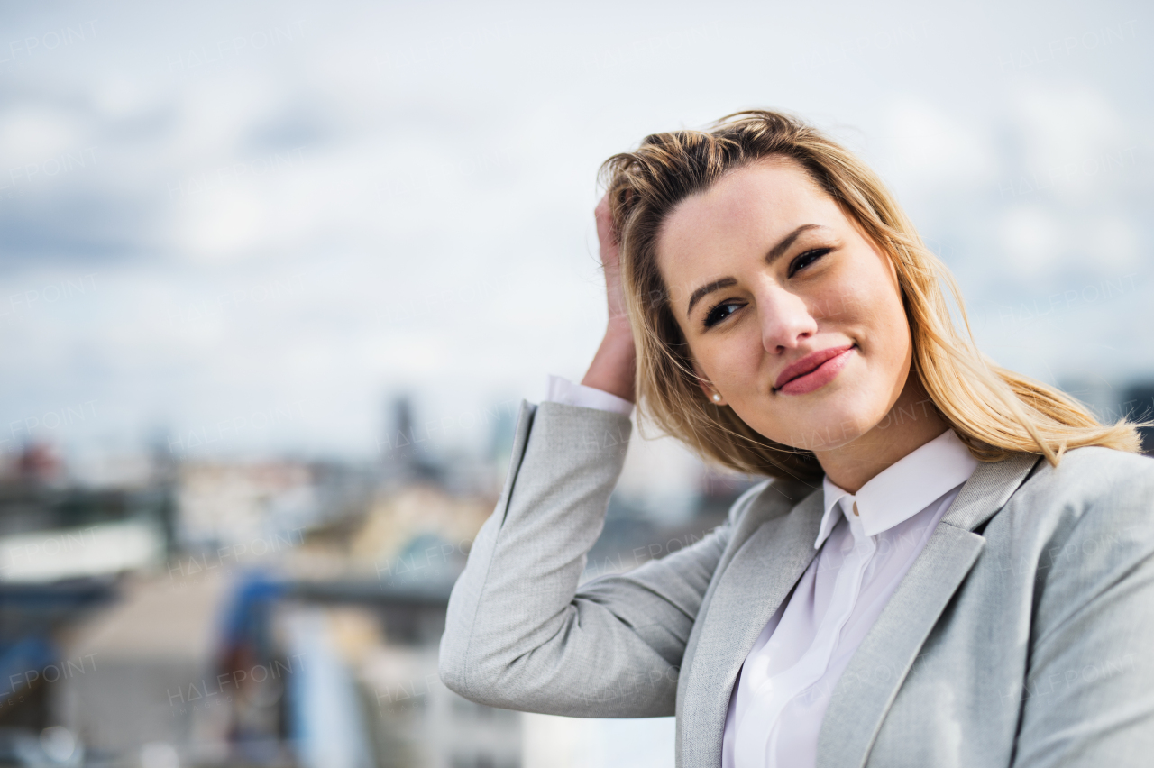 A portrait of young blond businesswoman standing outdoors on terrace outside office. Copy space.