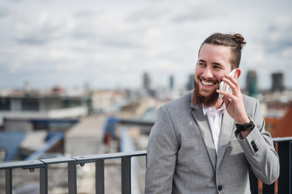 A young businessman with smartphone standing on a terrace outside office, making a phone call.