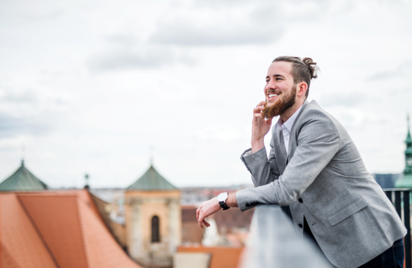 A young businessman with smartphone standing on a terrace outside office, making a phone call.