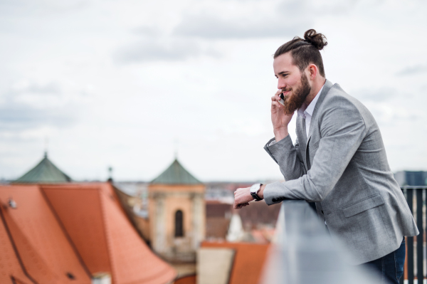 A young businessman with smartphone standing on a terrace outside office, making a phone call.