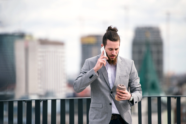 A young businessman with smartphone standing on a terrace outside office, making a phone call.