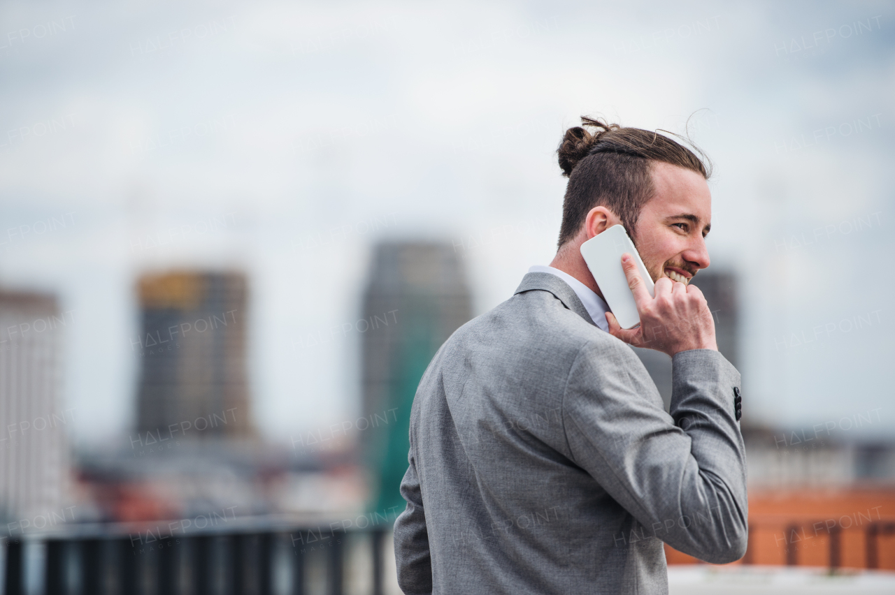 A young businessman with smartphone standing on a terrace outside office, making a phone call.