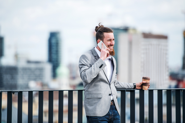 A young businessman with smartphone standing on a terrace outside office, making a phone call.