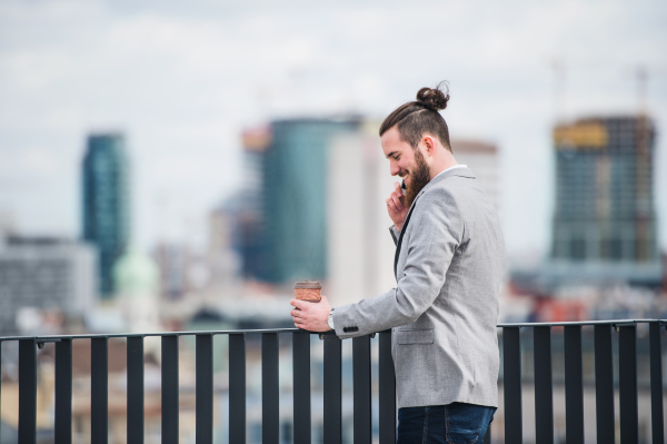 A young businessman with smartphone standing on a terrace outside office, making a phone call.