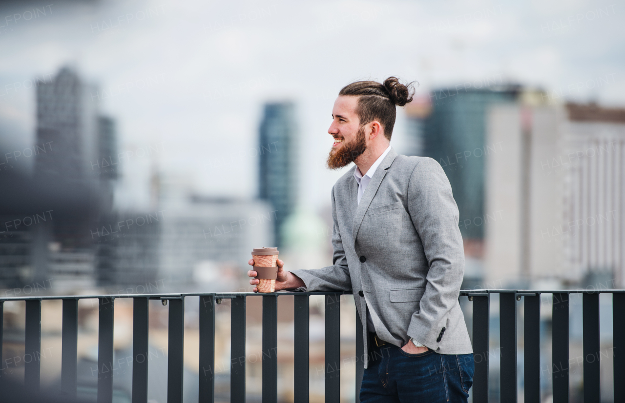 A young businessman with coffee standing on a terrace outside office, resting.