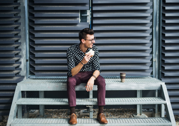 A young businessman with coffee and sandwich sitting outdoors, having a snack and resting.