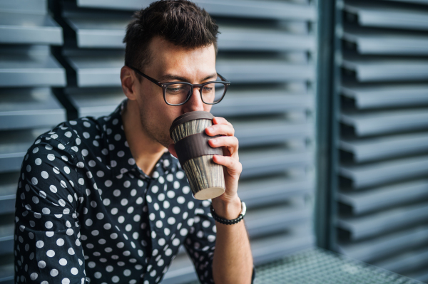 A young businessman sitting outdoors, drinking coffee. Copy space.