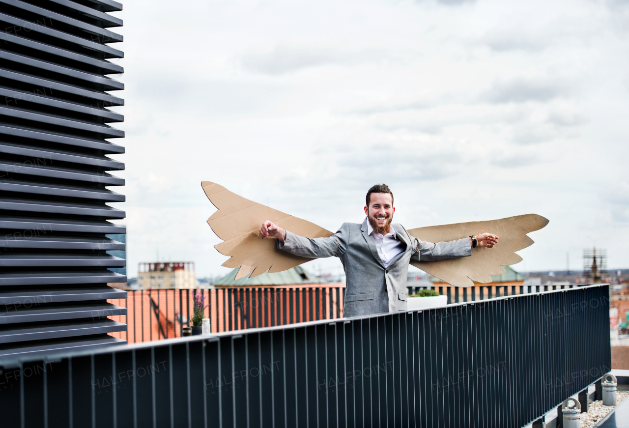 A young businessman with cardboard wings standing on a terrace, flying metaphor and freedom concept.