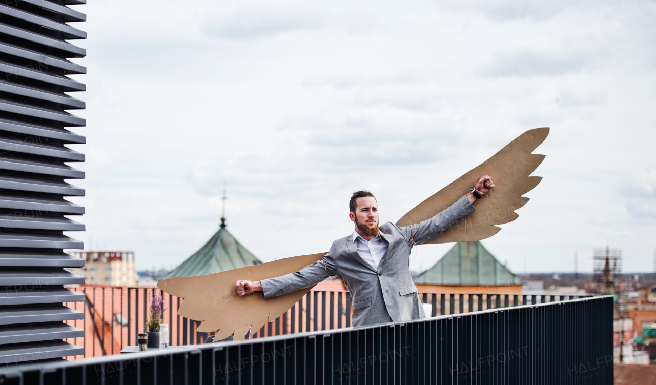 A young businessman with cardboard wings standing on a terrace, flying metaphor and freedom concept.