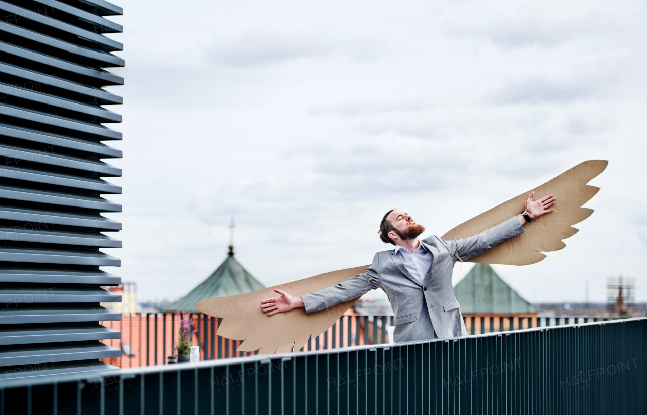 A young businessman with cardboard wings standing on a terrace, flying metaphor and freedom concept.