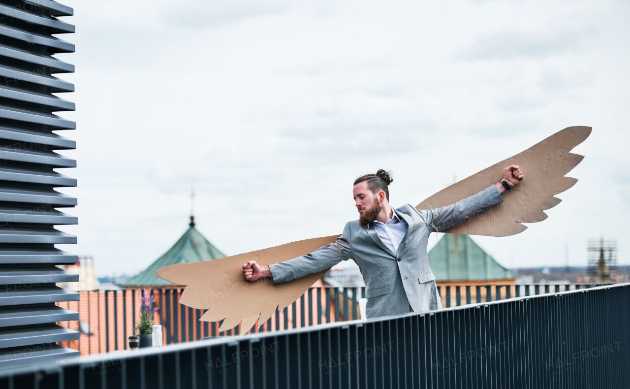 A young businessman with cardboard wings standing on a terrace, flying metaphor and freedom concept.