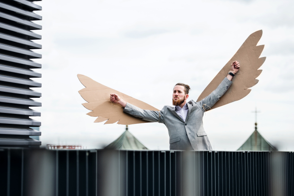 A young businessman with cardboard wings standing on a terrace, flying metaphor and freedom concept.