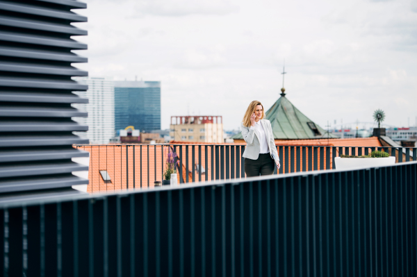 A young businesswoman with smartphone standing on a terrace, making a phone call.