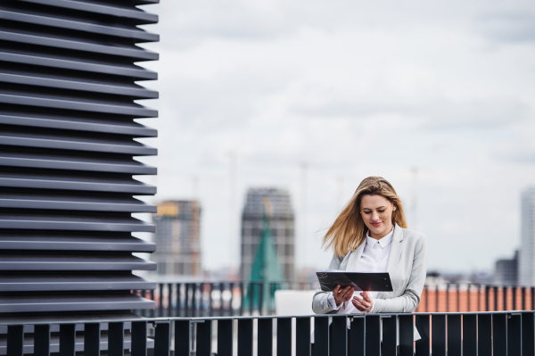 A young happy businesswoman with tablet standing on a terrace, working.