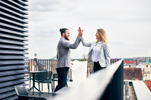 Two young business people with tablet standing on a terrace outside office, expressing excitement.