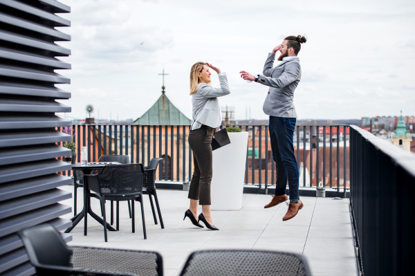 Two young business people with tablet standing on a terrace outside office, expressing excitement.