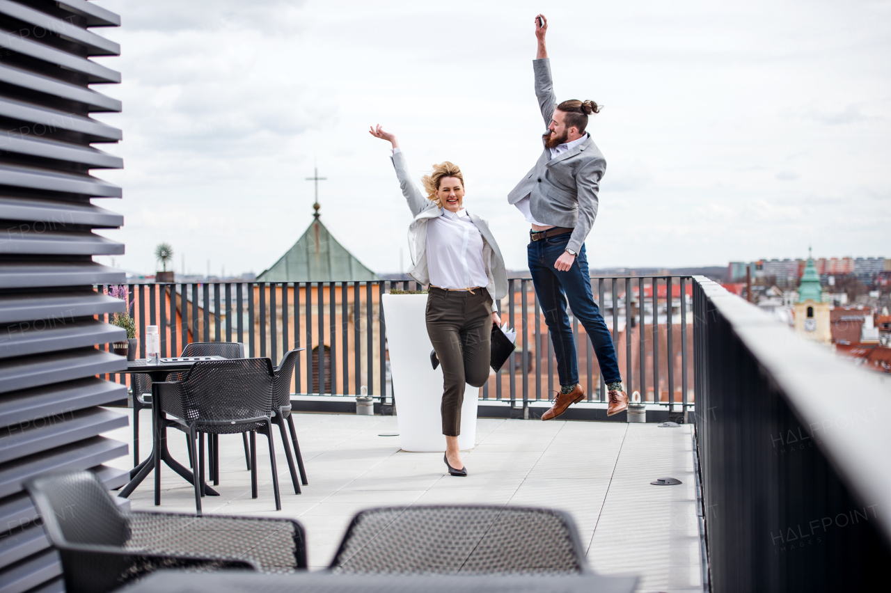 Two young business people jumping on a terrace outside office, expressing excitement.