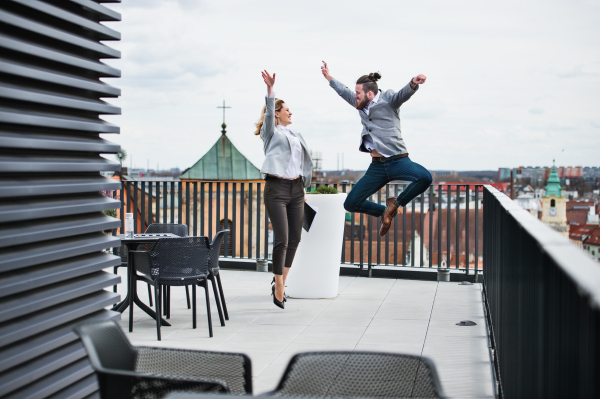 Two young business people with tablet standing on a terrace outside office, expressing excitement.