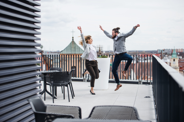 Two young business people jumping on a terrace outside office, expressing excitement.