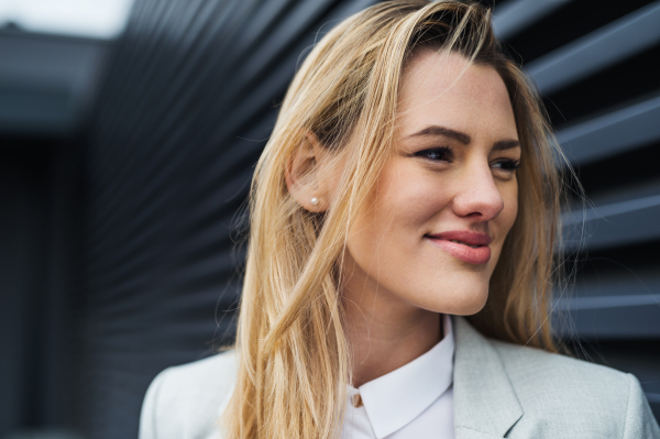 A close-up portrait of young blond businesswoman standing outdoors.