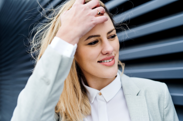 A close-up portrait of young blond businesswoman standing outdoors.