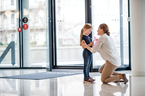 A mother saying goodbye to a small daughter in office building, nursery concept.