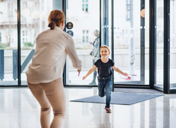 A rear view of businesswoman greeting with happy small daughter in office building.