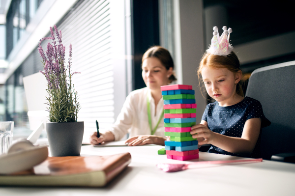 A businesswoman with a small daughter sitting in an office, working.