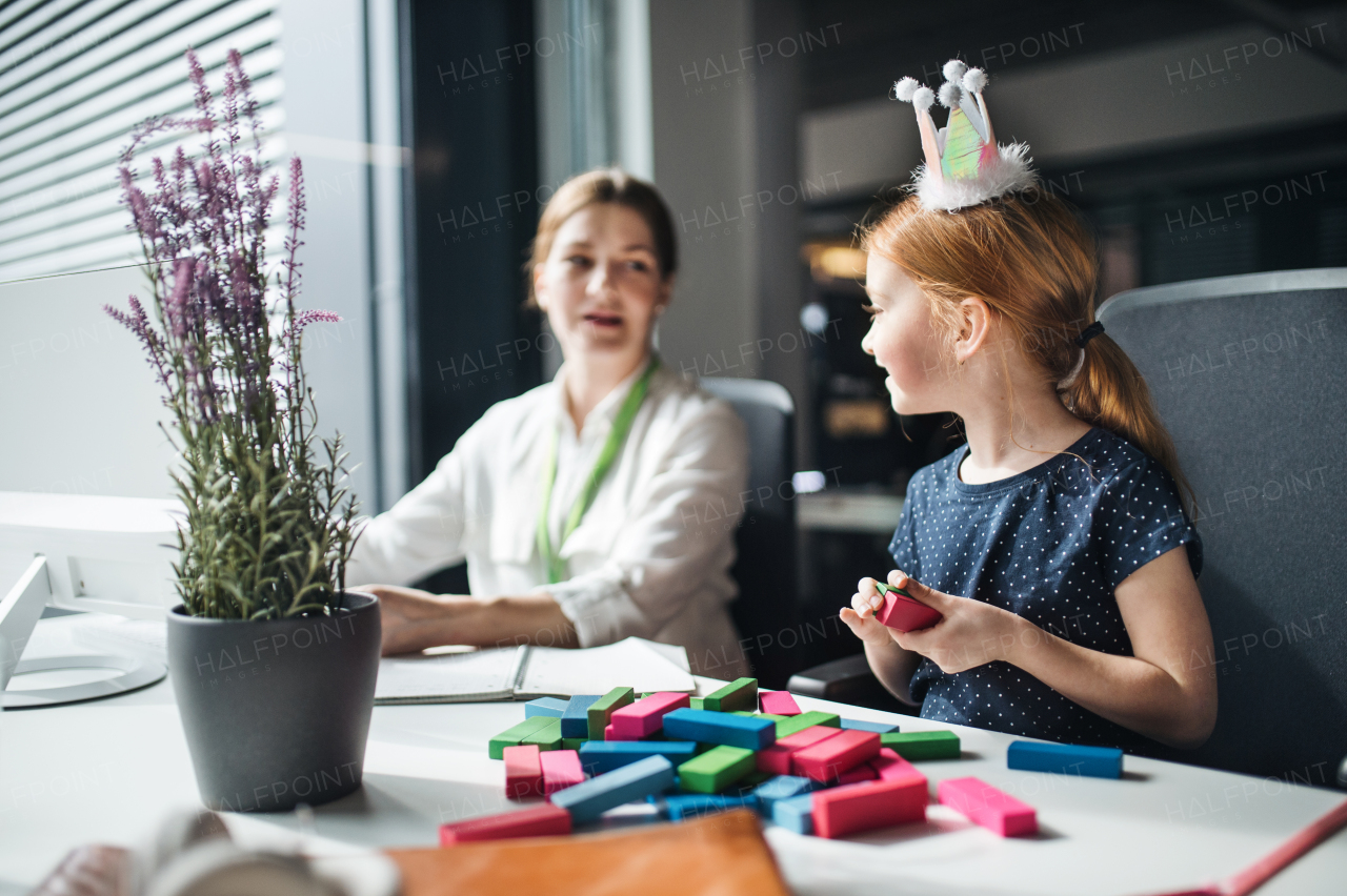 A businesswoman with a small daughter sitting in an office, working.