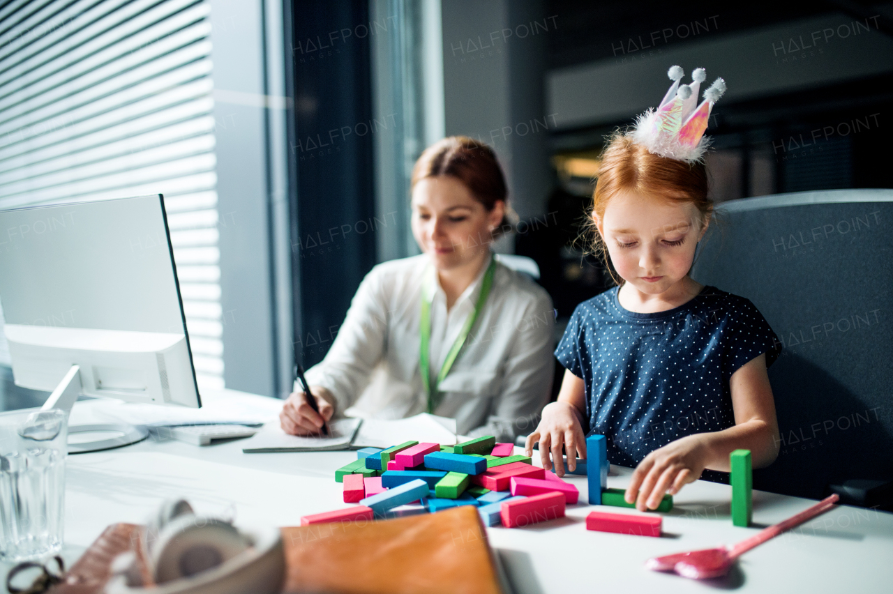 A businesswoman with a small daughter sitting in an office, working.