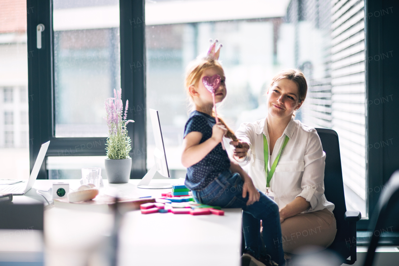 A businesswoman with a small daughter sitting in an office, working and playing.