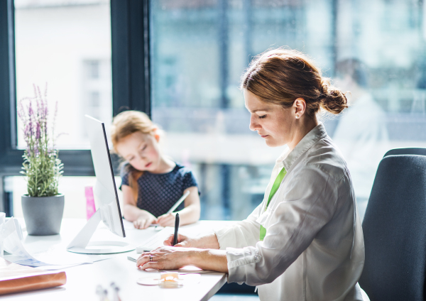 A businesswoman with a small daughter sitting in an office, working.