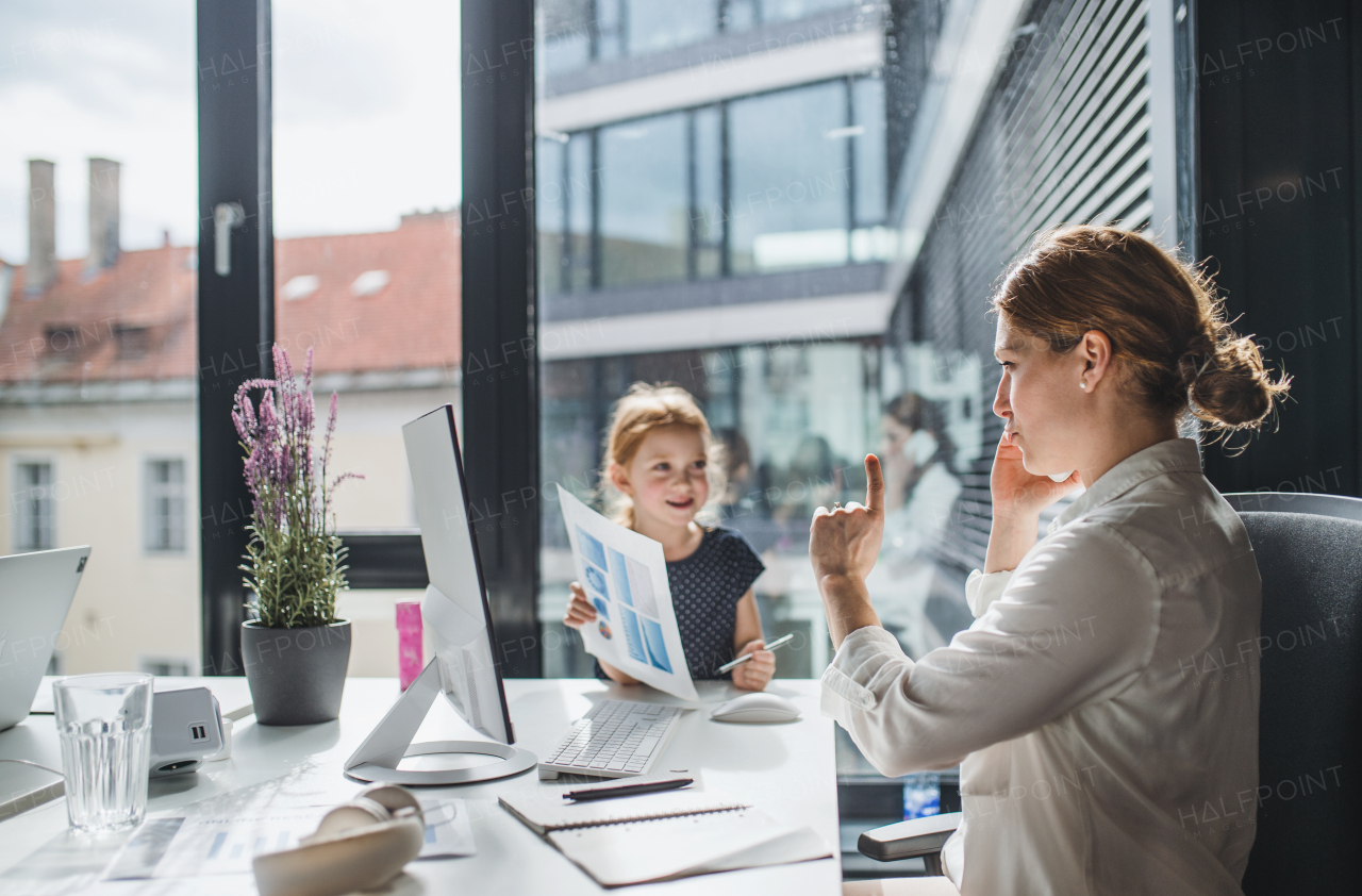 A businesswoman with a small daughter sitting in an office, working.