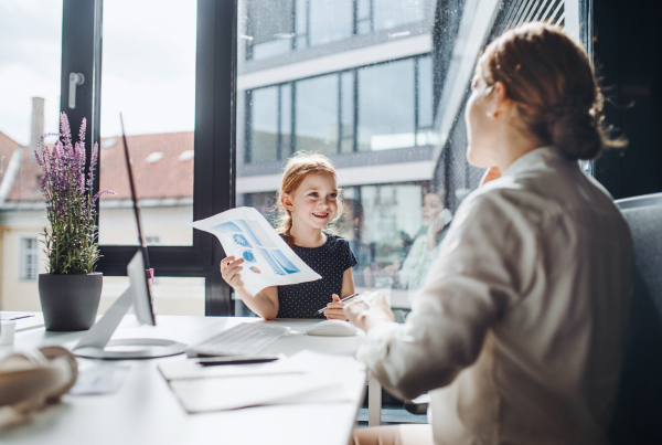 A businesswoman with a small daughter sitting in an office, working.