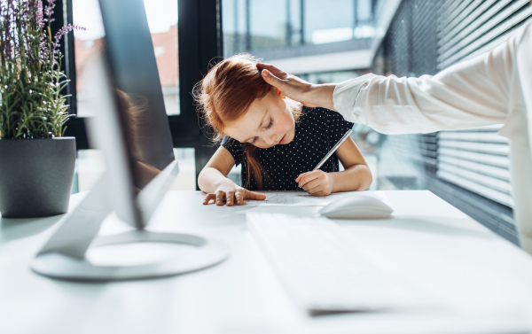 A midsection of businesswoman with a small daughter sitting in an office, working.