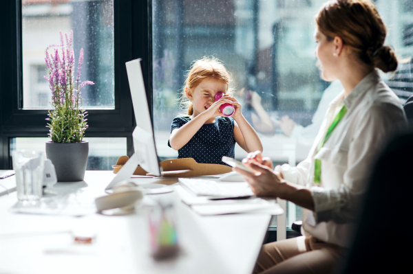 A businesswoman with a small daughter sitting in an office, working and playing.