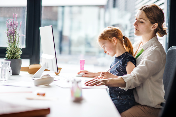 A businesswoman with a small daughter sitting in an office, working.