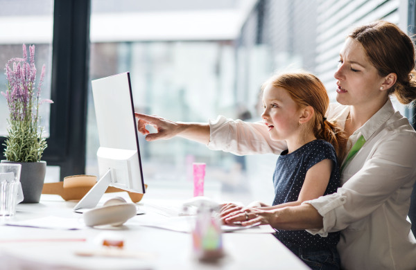 A businesswoman with a small daughter sitting in an office, working.