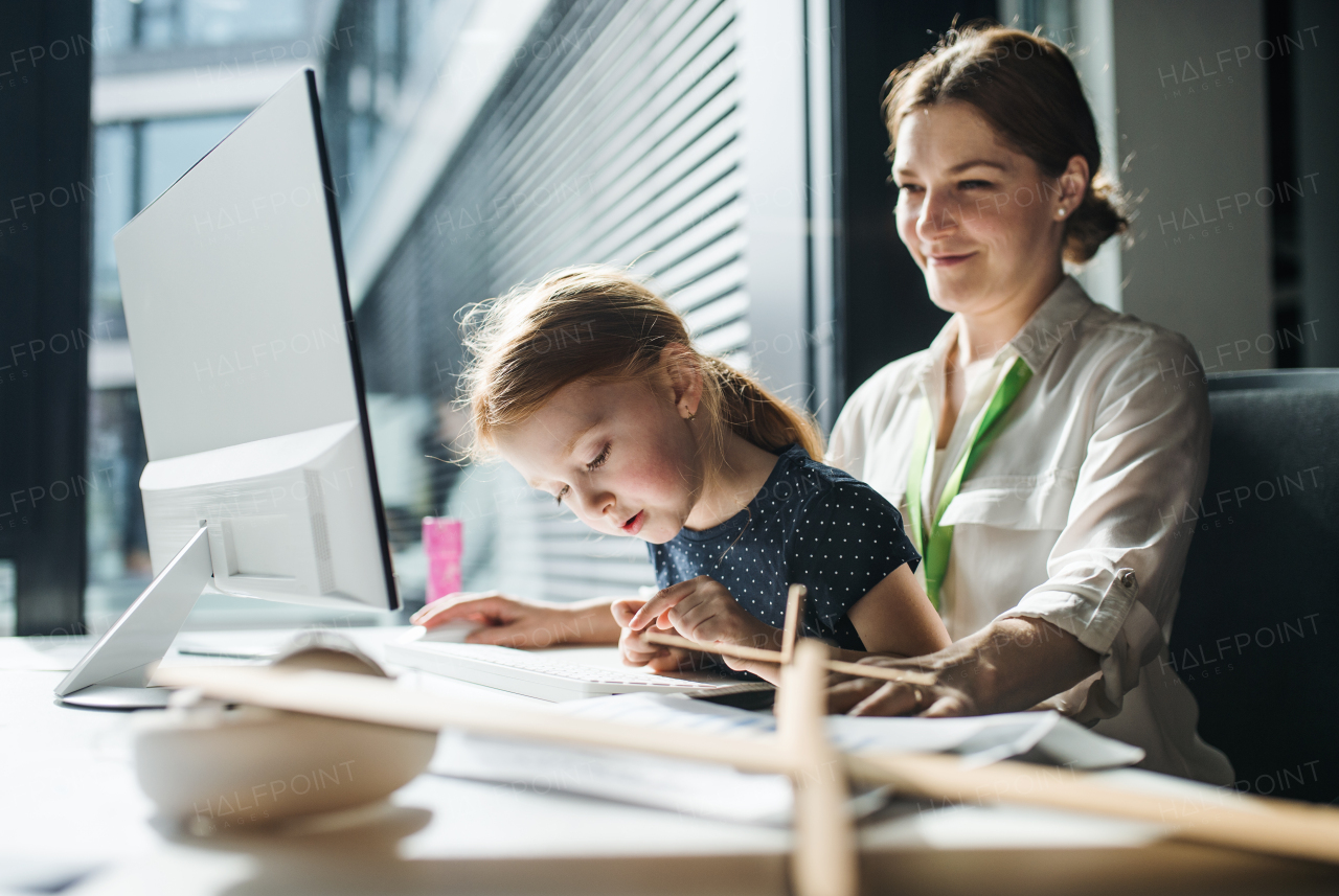 A businesswoman with a small daughter sitting in an office, working.