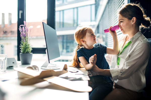 A businesswoman with a small daughter sitting in an office, working and playing.